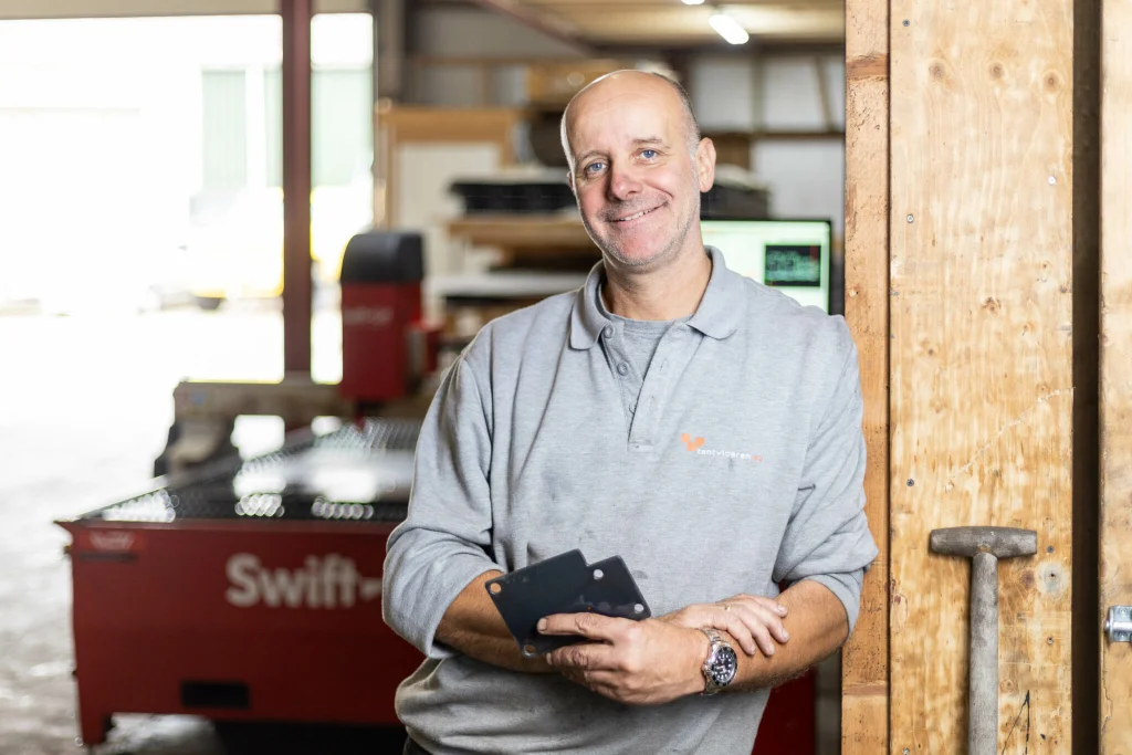 Peter, en representación de Tentvloeren, de pie frente a su mesa de corte por plasma CNC Swift-Cut Pro, sosteniendo piezas metálicas que ha cortado en la propia mesa