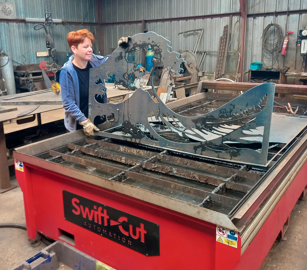 IJA Ferronnerie holding up piece of cut metal of Japanese wave design. cut on a Swift-Cut Pro 3000 CNC plasma cutting machine